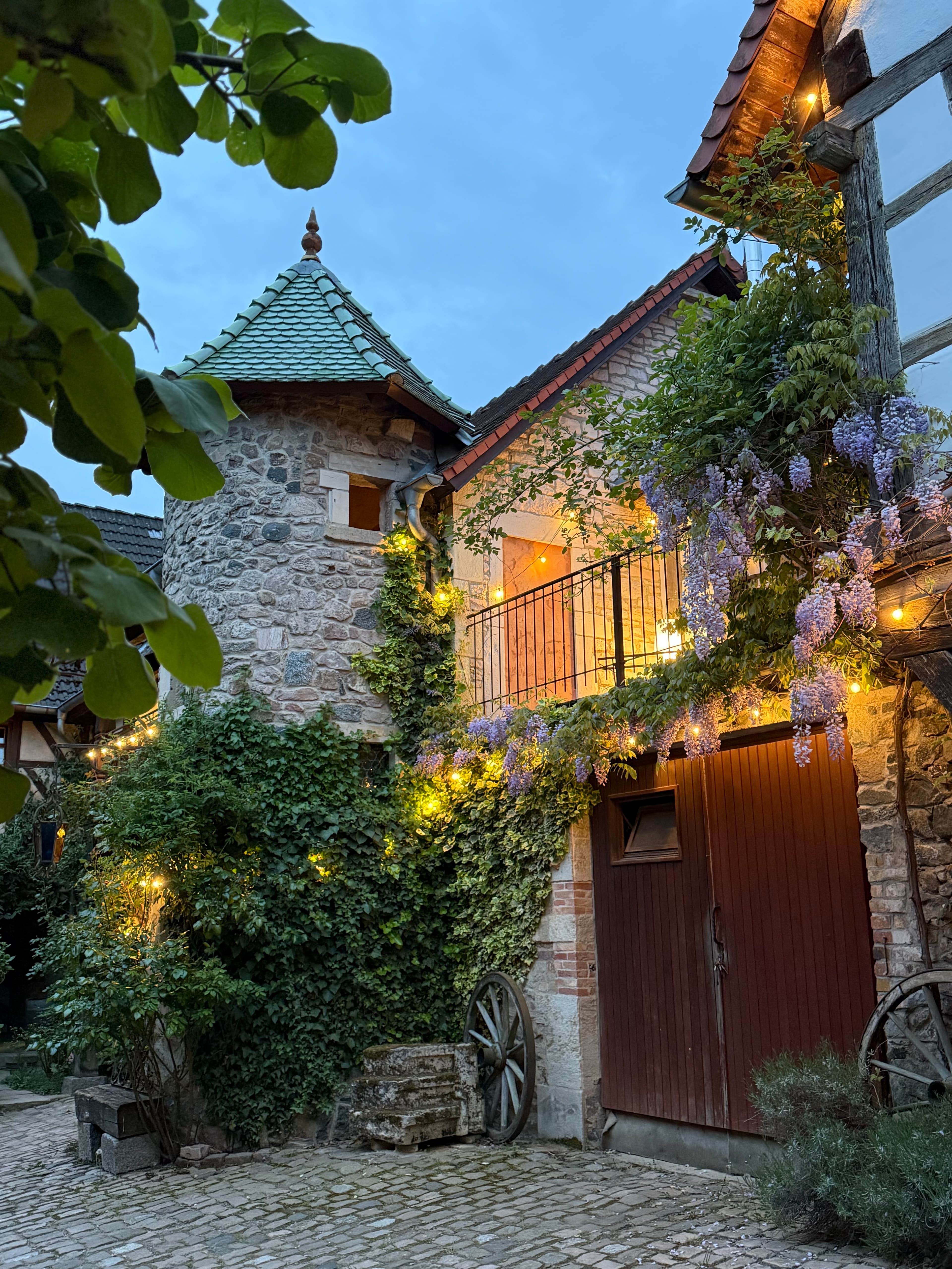 Historischer Innenhof mit Turm, Lichterketten und Glyzinien am Abend