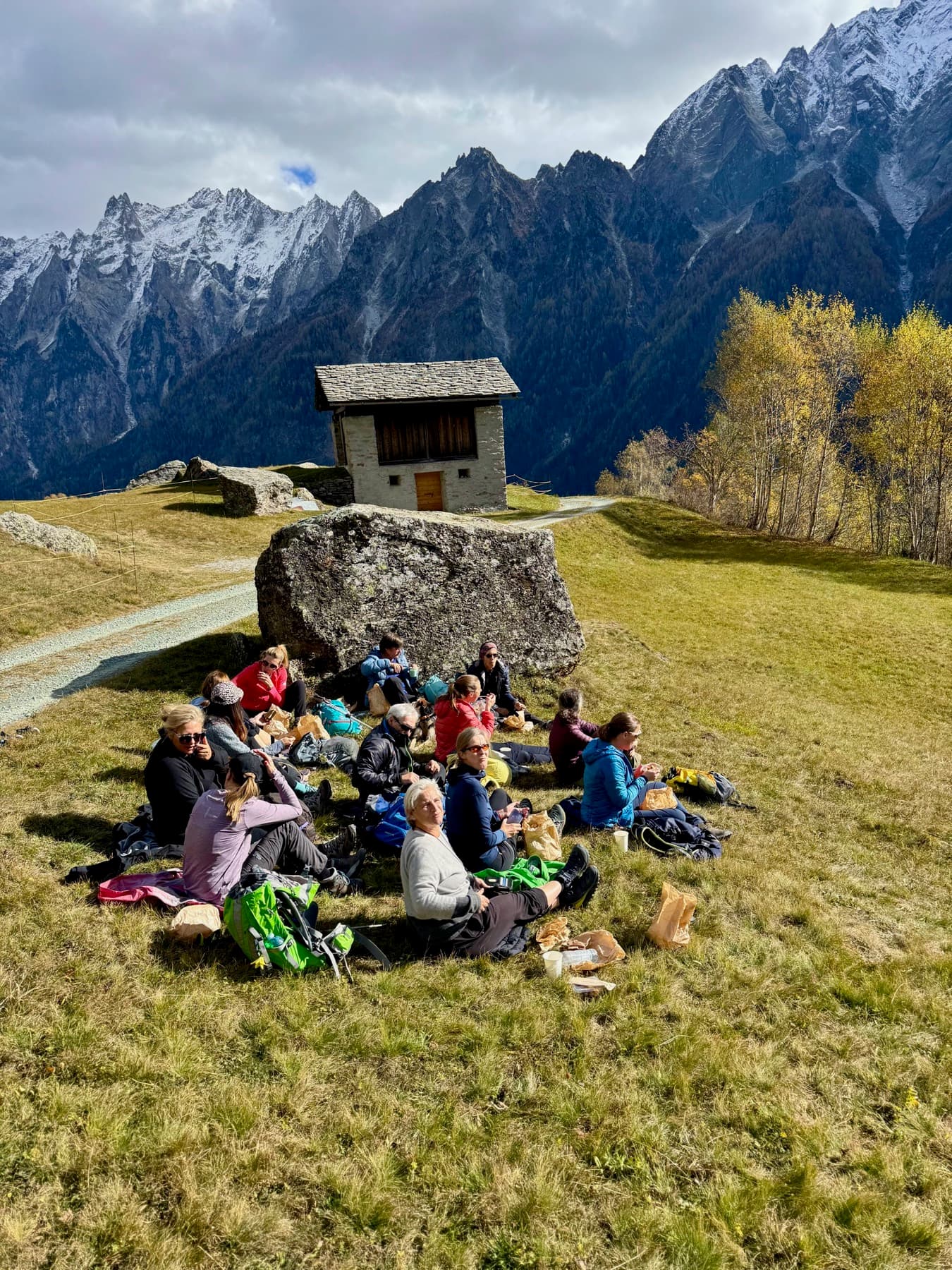 Retreat-Gruppe beim Picknick auf einer Alm vor schneebedeckten Gipfeln